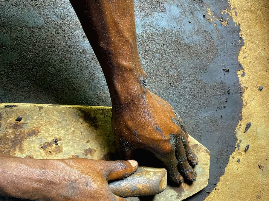 Artisan hands applying earthen plaster finish with a wooden trowel